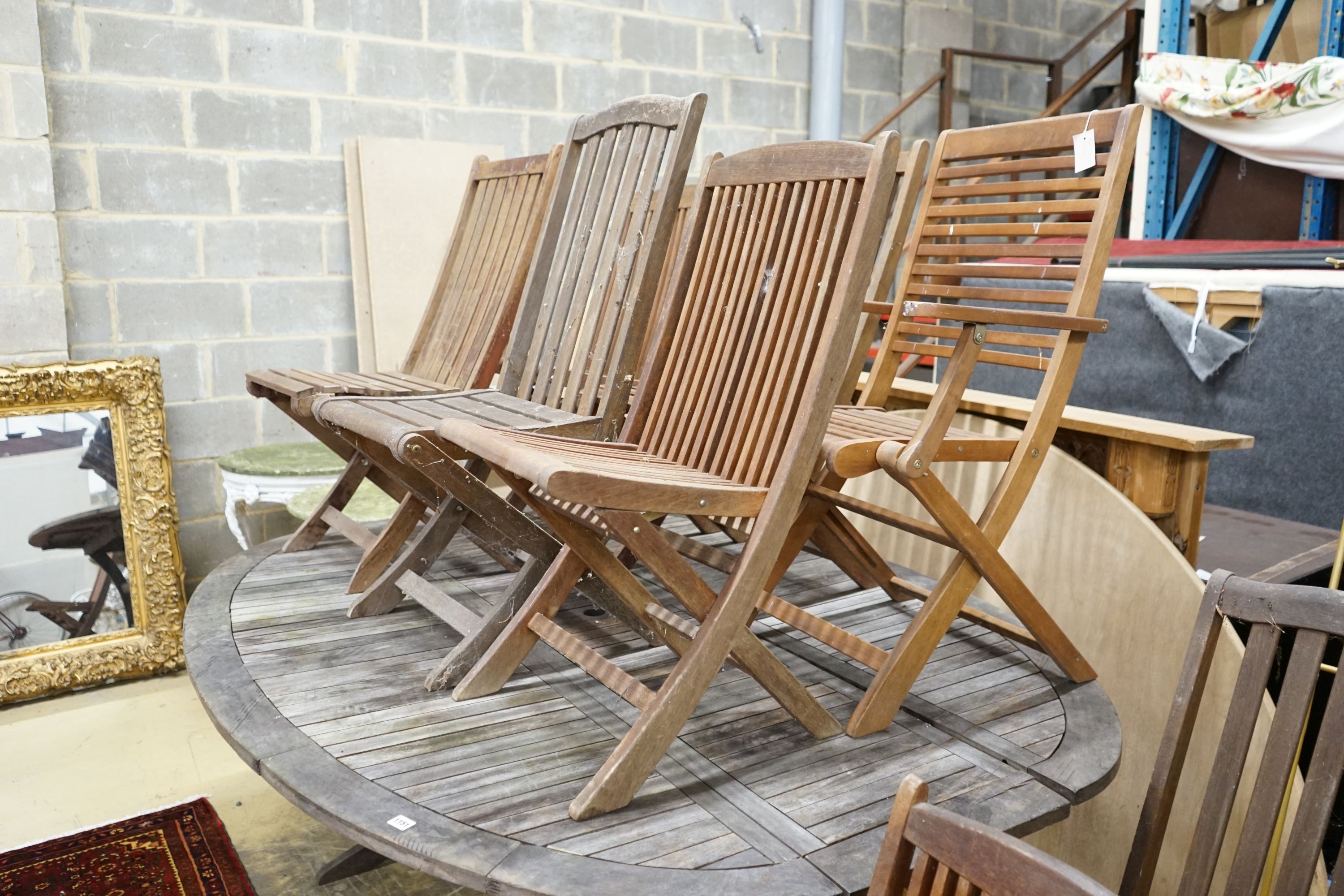 A large weathered oval teak extending garden table, length 200cm extended, height 151cm together with and eight folding teak garden chairs